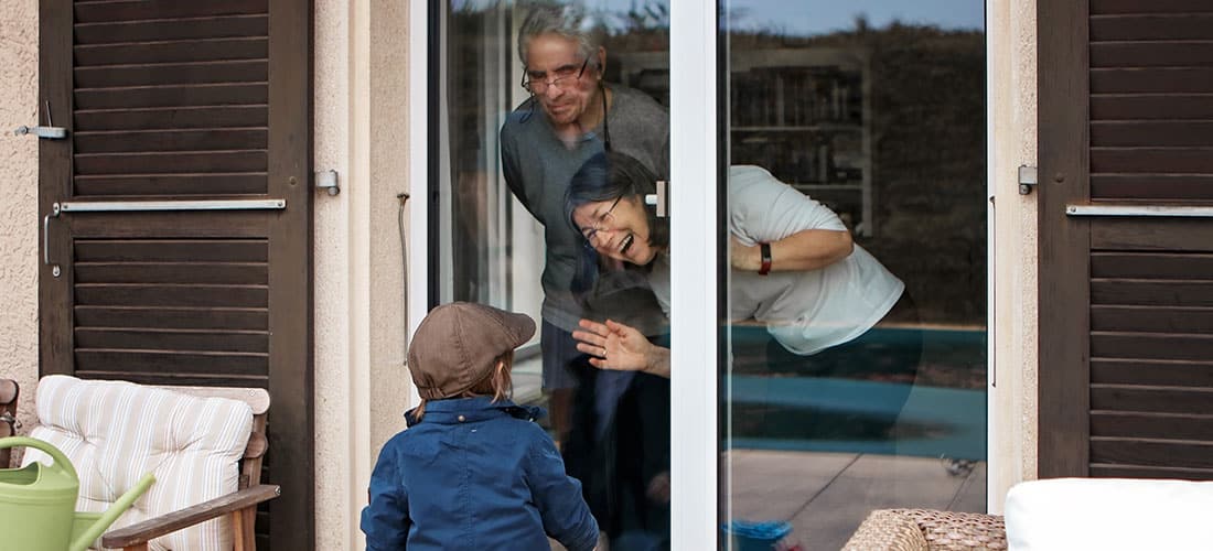 Grandparents saying hi to their grandchild through their glass door.