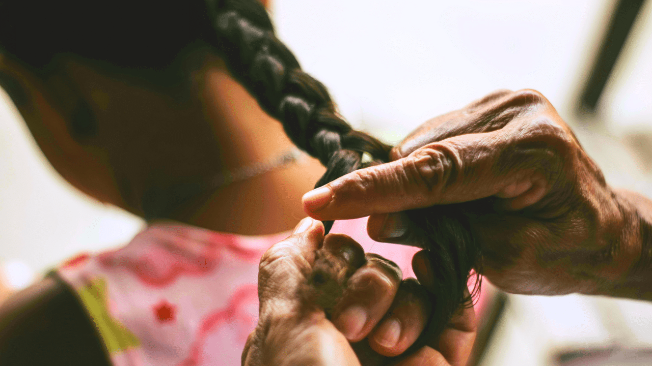 A Black grandmother braids her grandaughter's hair.