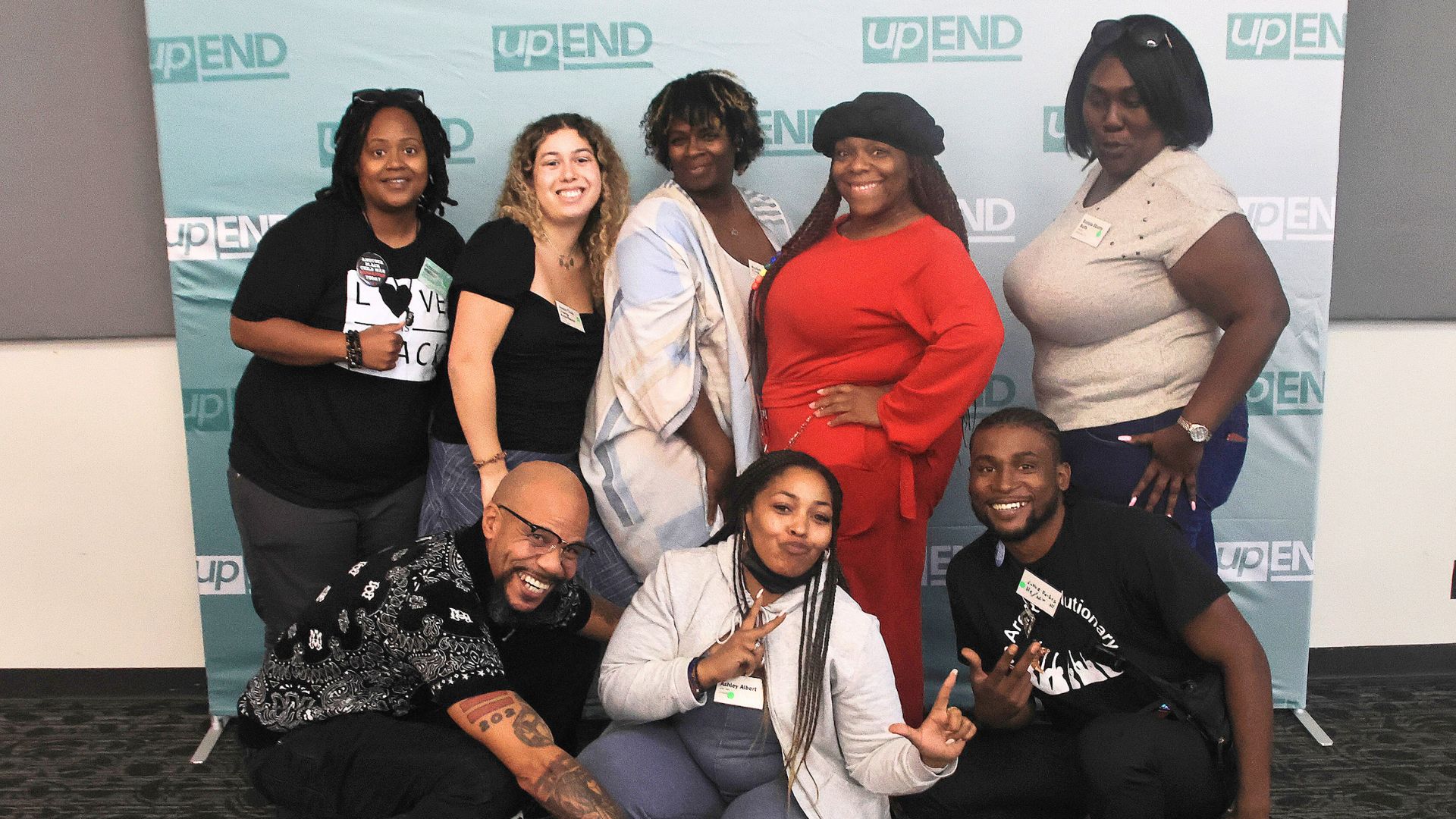 A group photo of participants at the upEND 2024 Convening are smiling and standing in front of a green upEND banner.