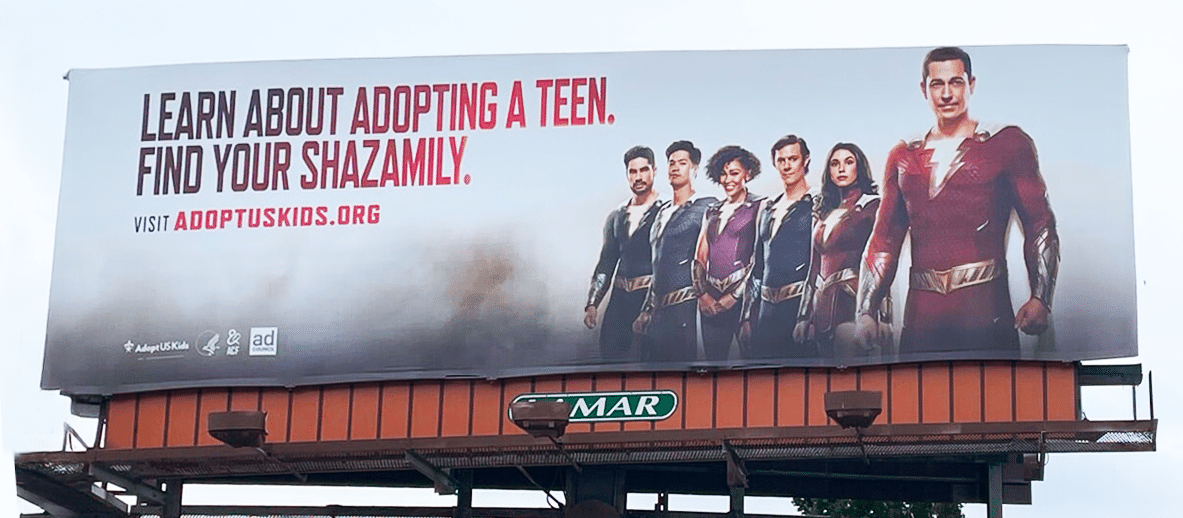 A billboard features the cast of Shazam! Fury of the Gods (2023) and reads: “Learn about adopting a teen. Find your Shazamily. Visit adoptuskids.org” 