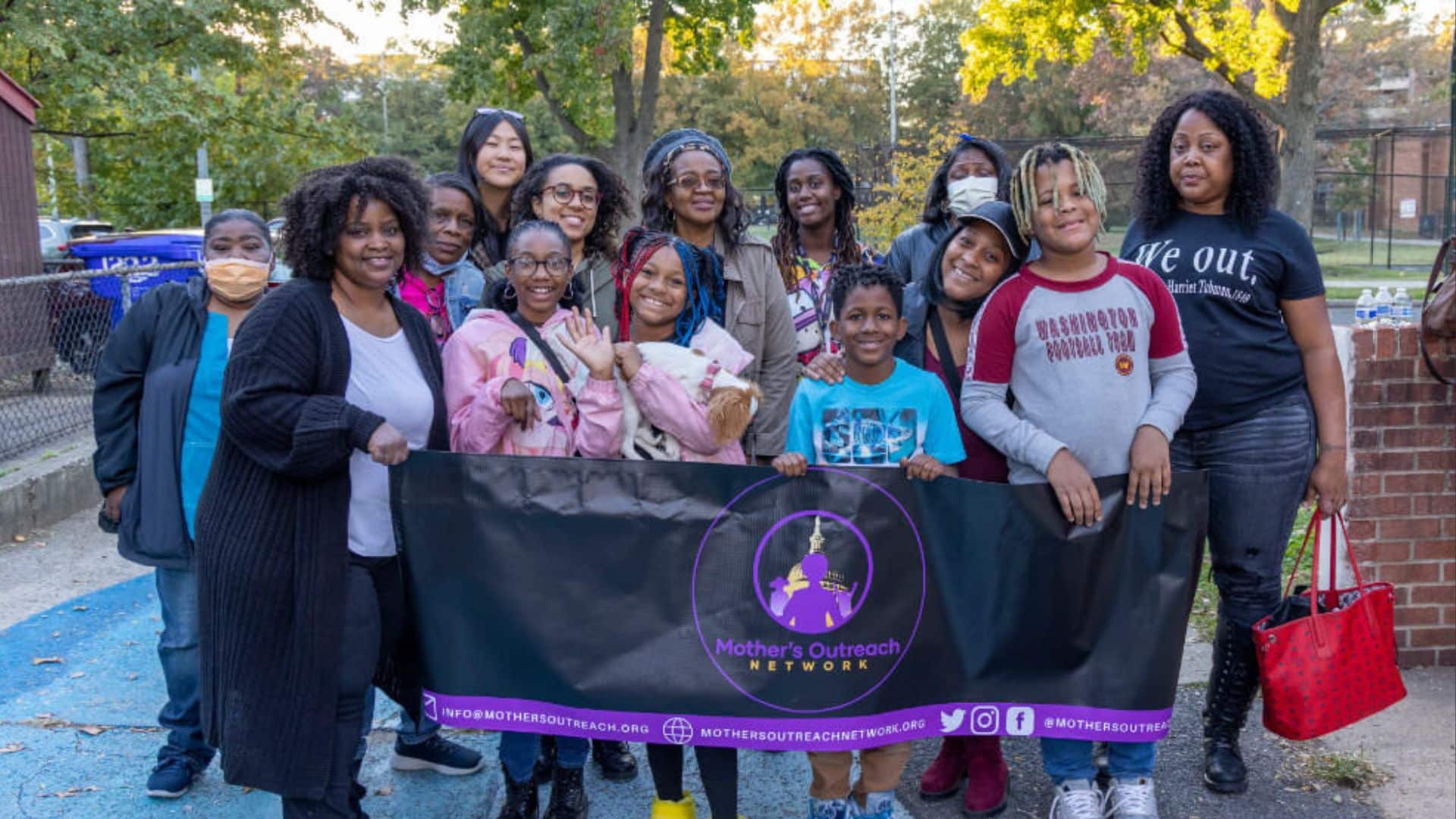 A group photo of Black women and girls holding a Mothers Outreach Network banner.